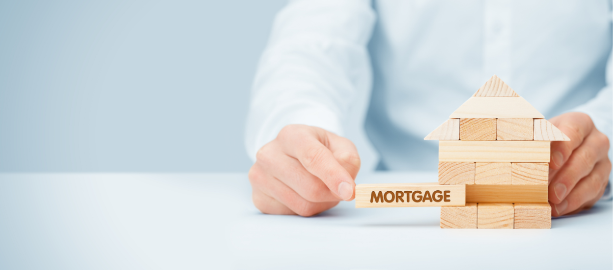 Man playing with jenga pieces in the shape of a house. One of pieces says Mortgages on it.