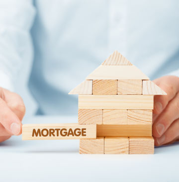 Man playing with jenga pieces in the shape of a house. One of pieces says Mortgages on it.